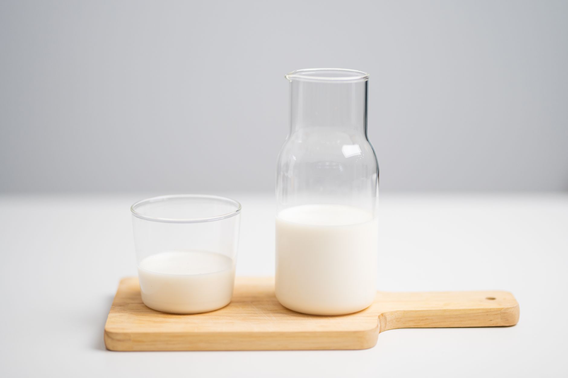 牛乳とミルクピッチャーを木のボードに並べた、明るく清潔な食卓のイメージ