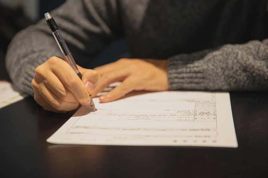 書類に記入して申請の手続きをする手元のイメージ（顔なし）