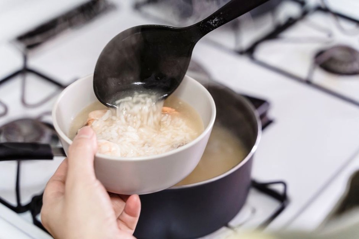 おたまですくったごはんを白い器によそう手元。明るいキッチンのコンロの上