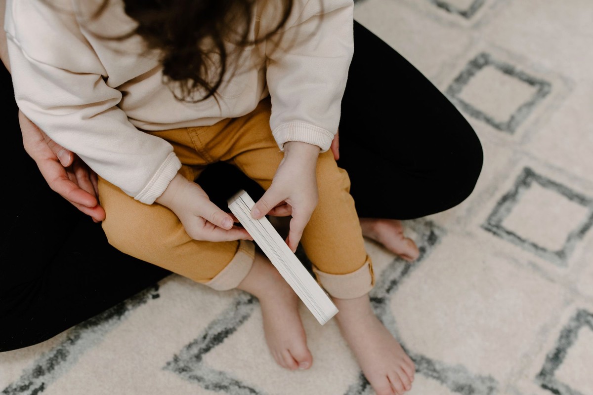 ラグに座った保護者のひざの上で、小さな本を両手で持っている子どもの手元