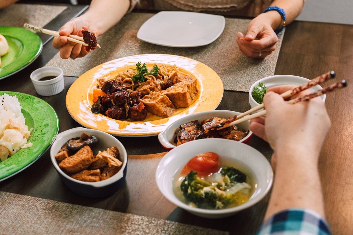 食卓に冷奴や煮物、青菜、汁物などの小鉢が並び、箸を伸ばす手が写っている家庭の食事の場面