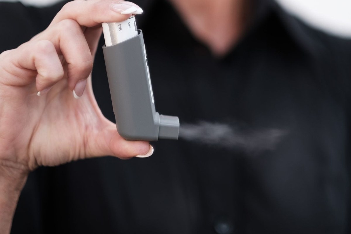 手に持った定量噴霧式吸入器(pMDI)から薬剤が霧状に噴霧されている様子