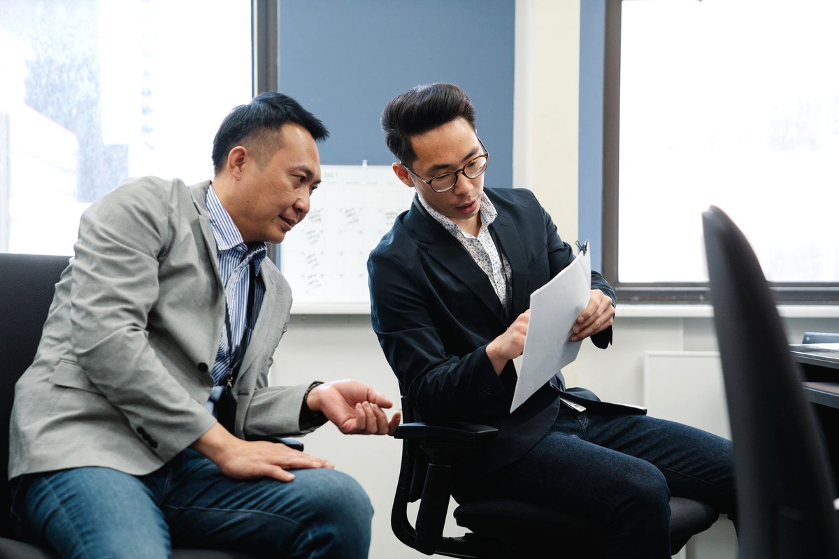 明るいオフィスの窓辺で書類を見ながら落ち着いて話し合う東アジア系の男性2人