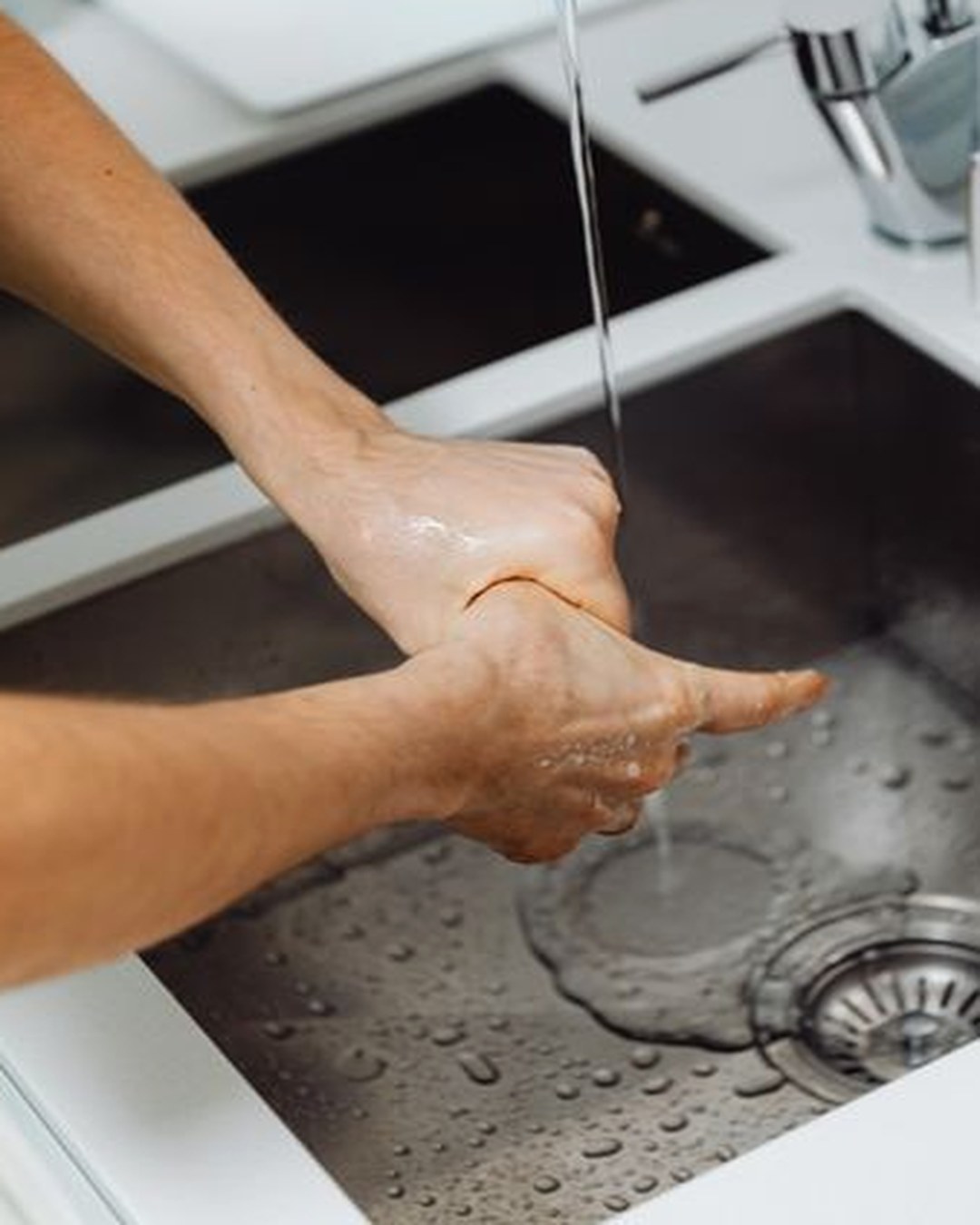 明るいキッチンのシンクで、蛇口から流れる水道水に指先を当てて洗っている手元