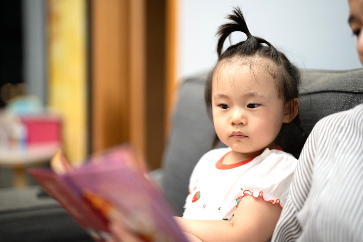 소파에 앉은 아이 곁에서 보호자가 그림책을 읽어 주며 함께 시간을 보내는 모습