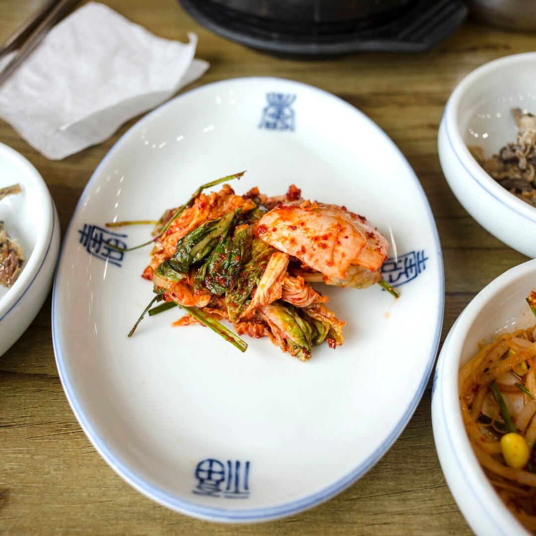 흰 접시에 담긴 파김치와 곁들여 놓인 한국식 밑반찬 그릇들