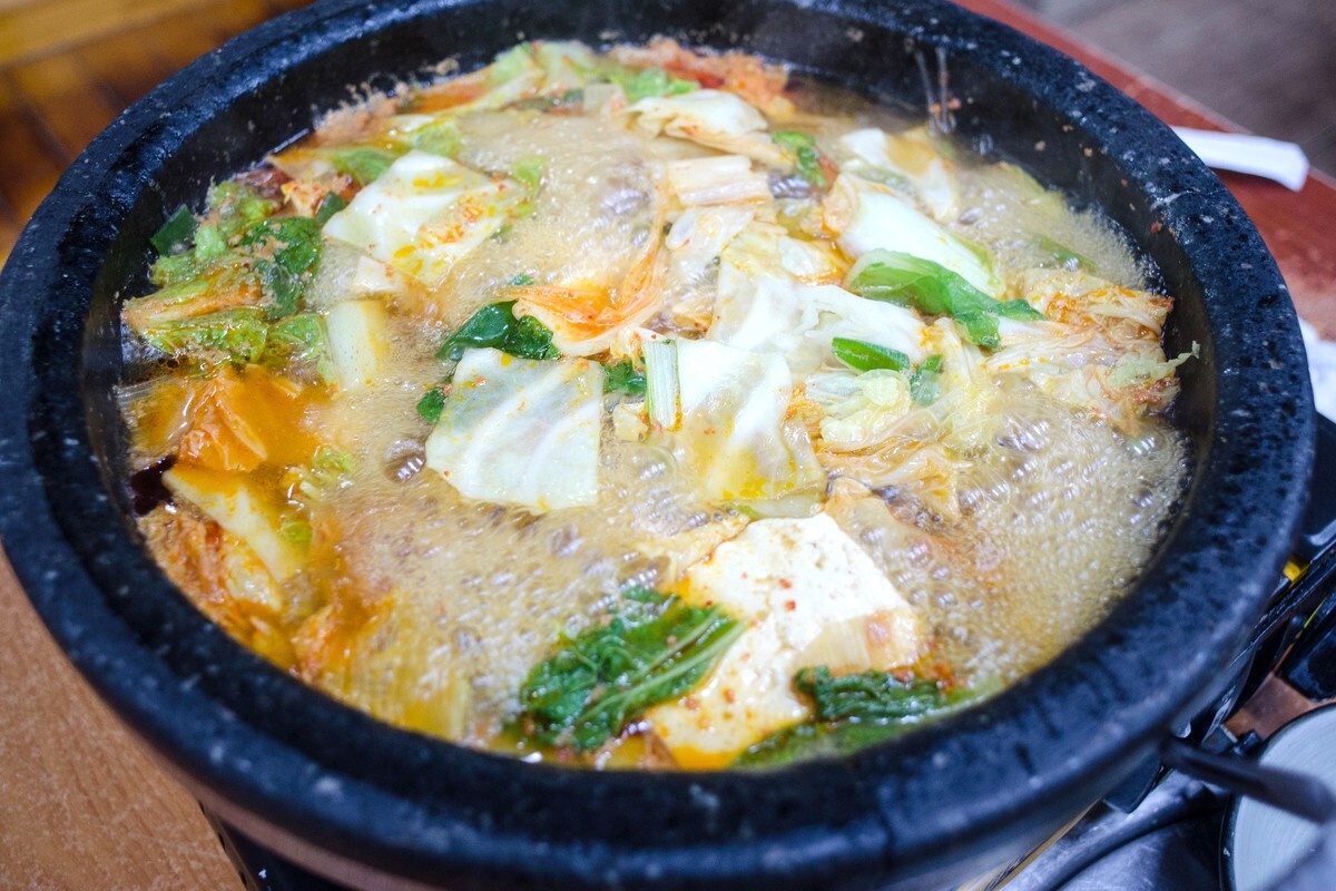 돌솥에 담긴 김치찌개가 가장자리부터 가운데까지 전체가 보글보글 끓어오르는 모습을 가까이에서 찍은 사진