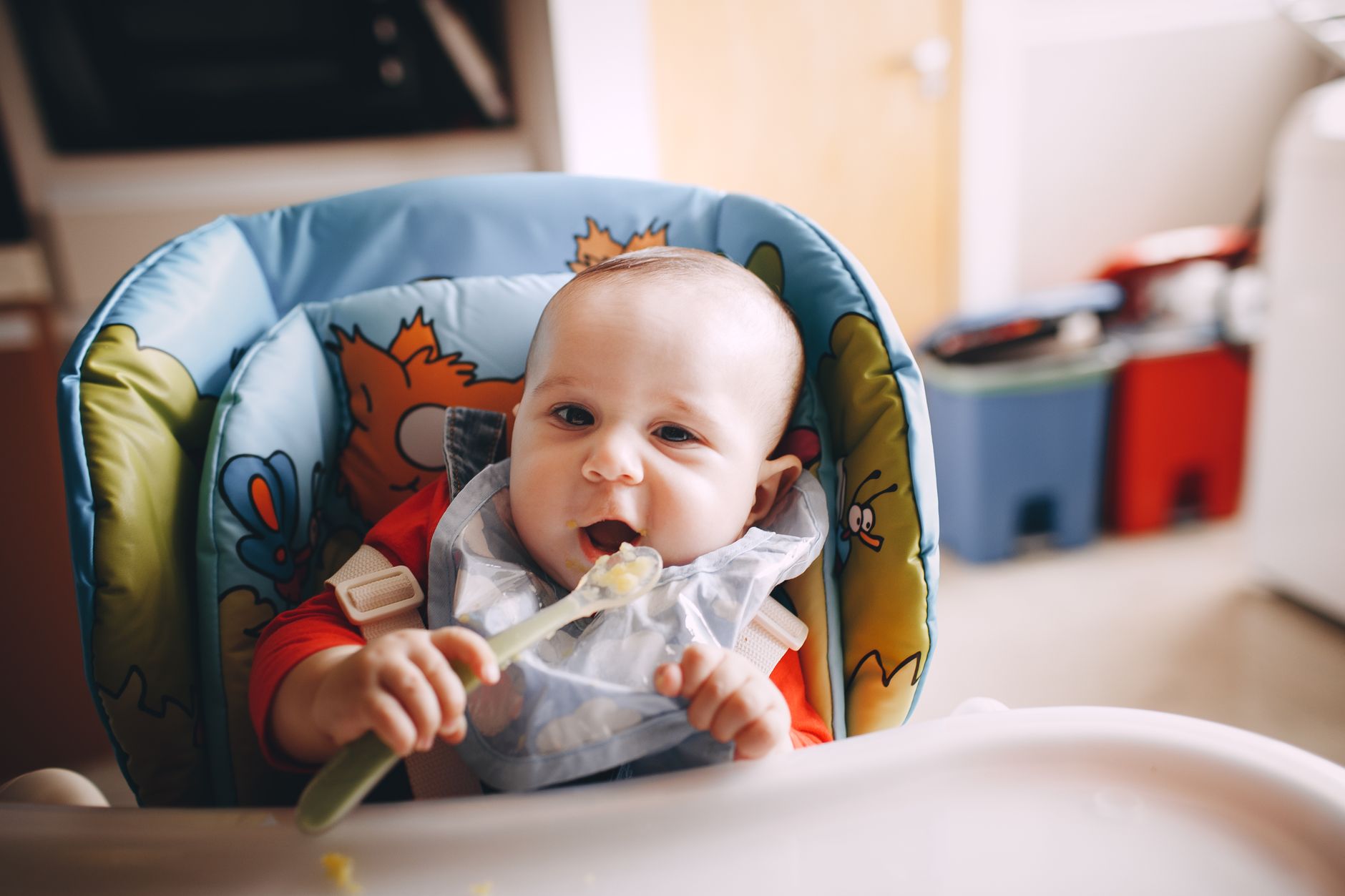 A baby in a high chair eating a spoonful of first solids