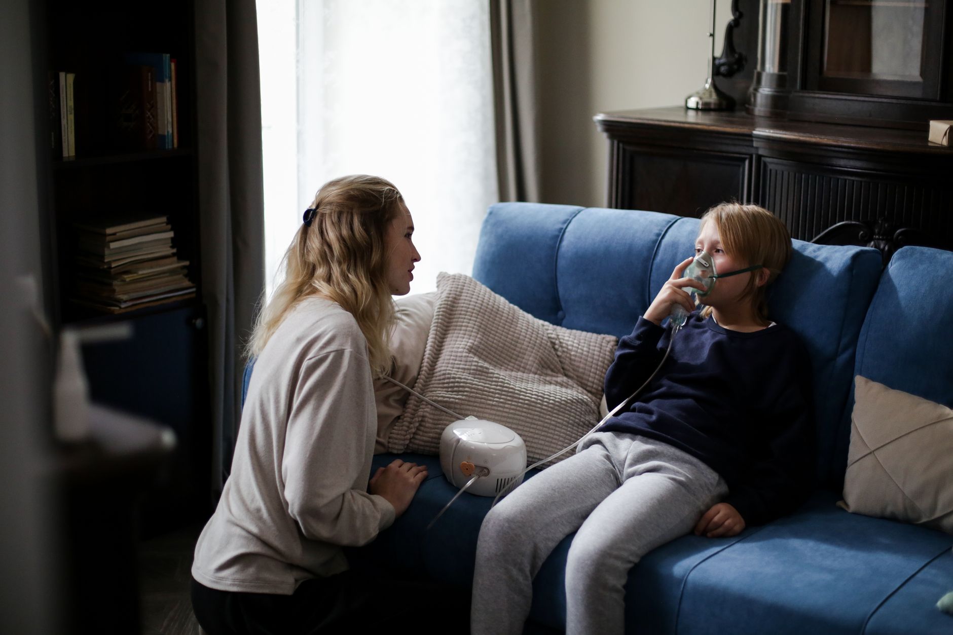 Parent staying close while a young child receives a quiet home nebulizer treatment on the couch