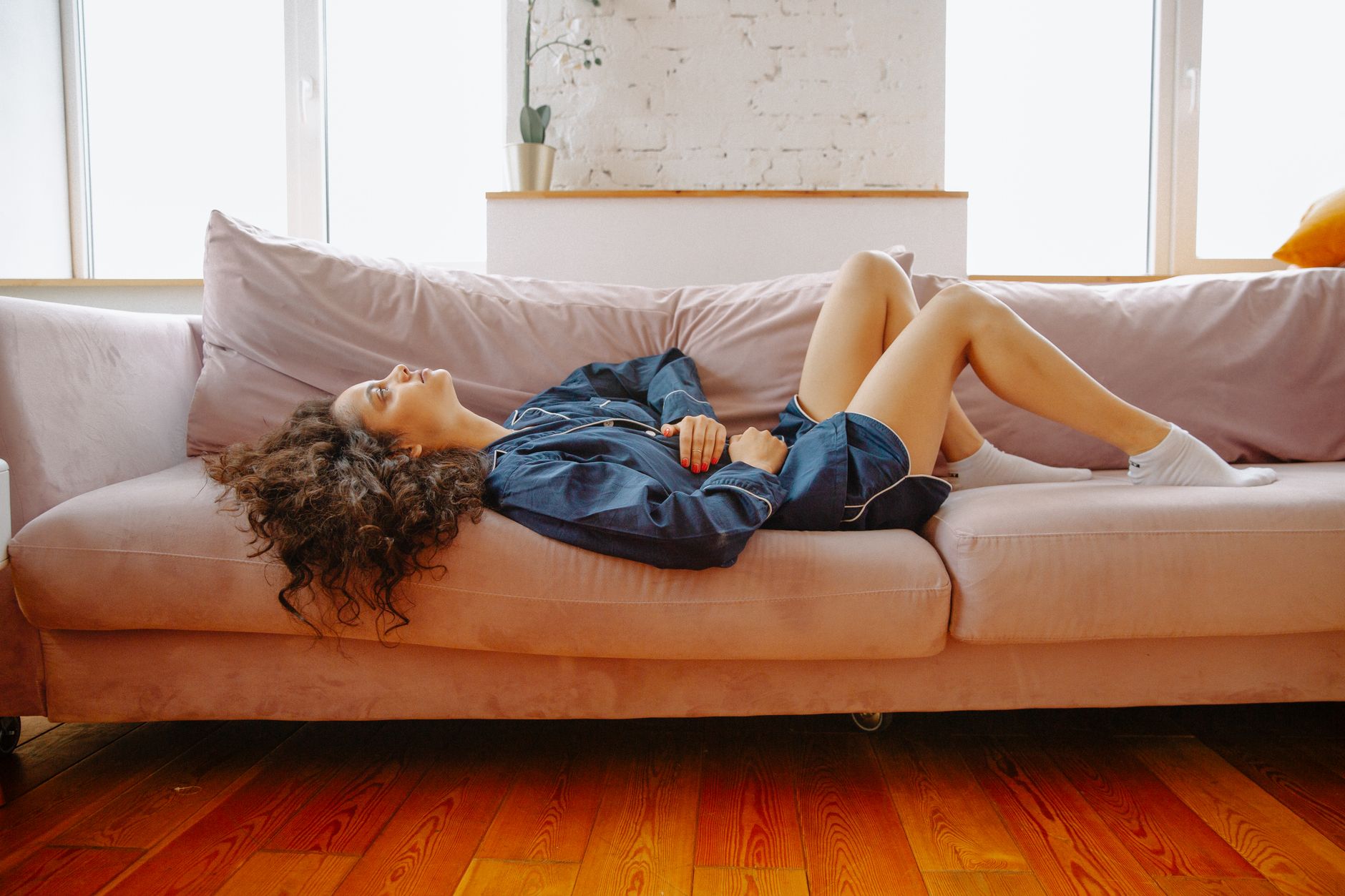 A woman in casual clothes resting on a couch with abdominal discomfort in soft daylight