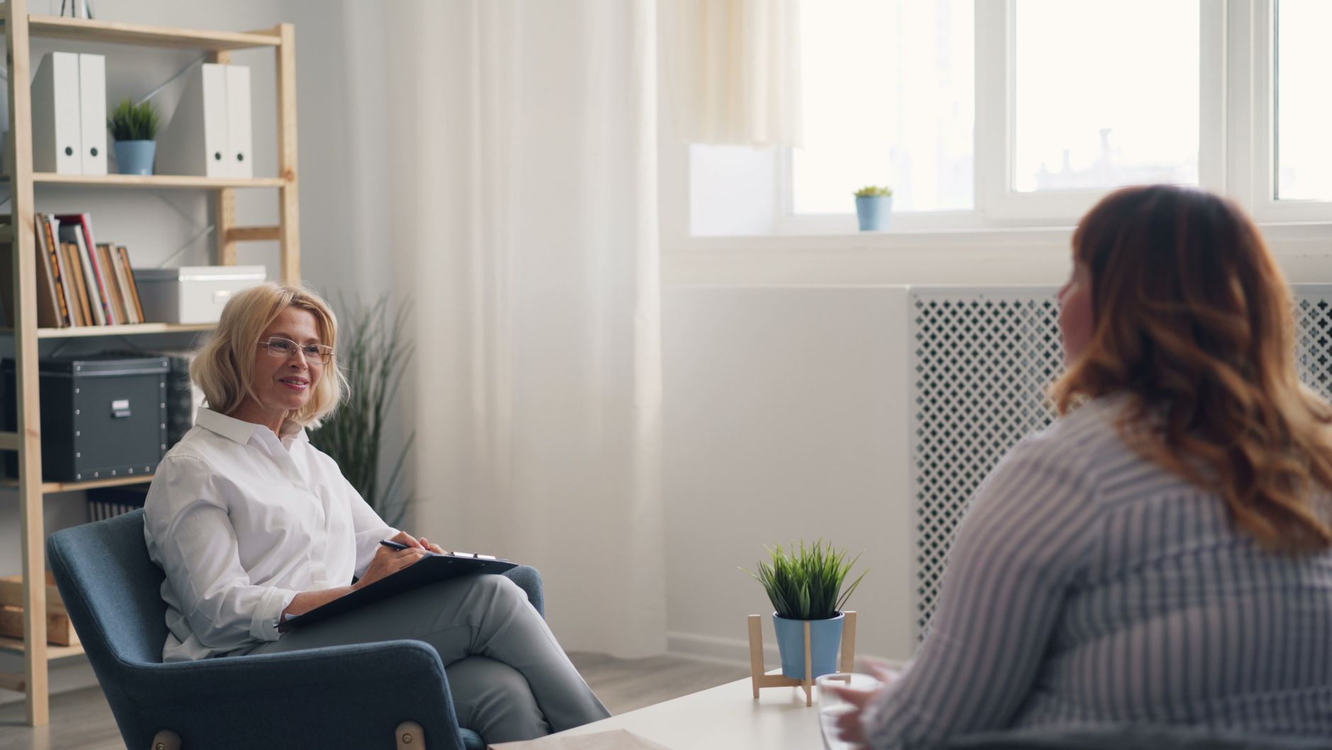 A therapist with a notepad listens to a client during a calm, bright counseling session
