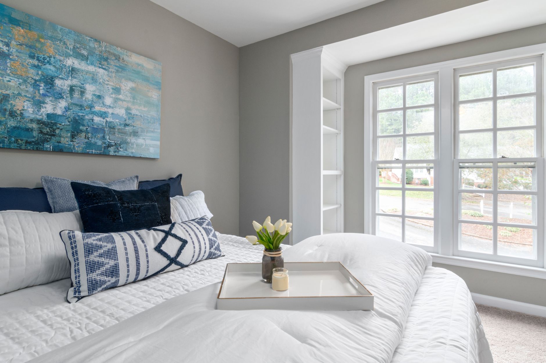 A bright, airy bedroom with pillows on a neatly made bed by a sunny window