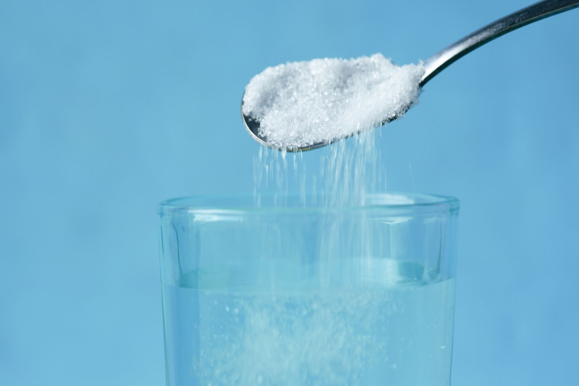 A spoon adding fine salt to a glass of water to make an isotonic, roughly 0.9% saline solution