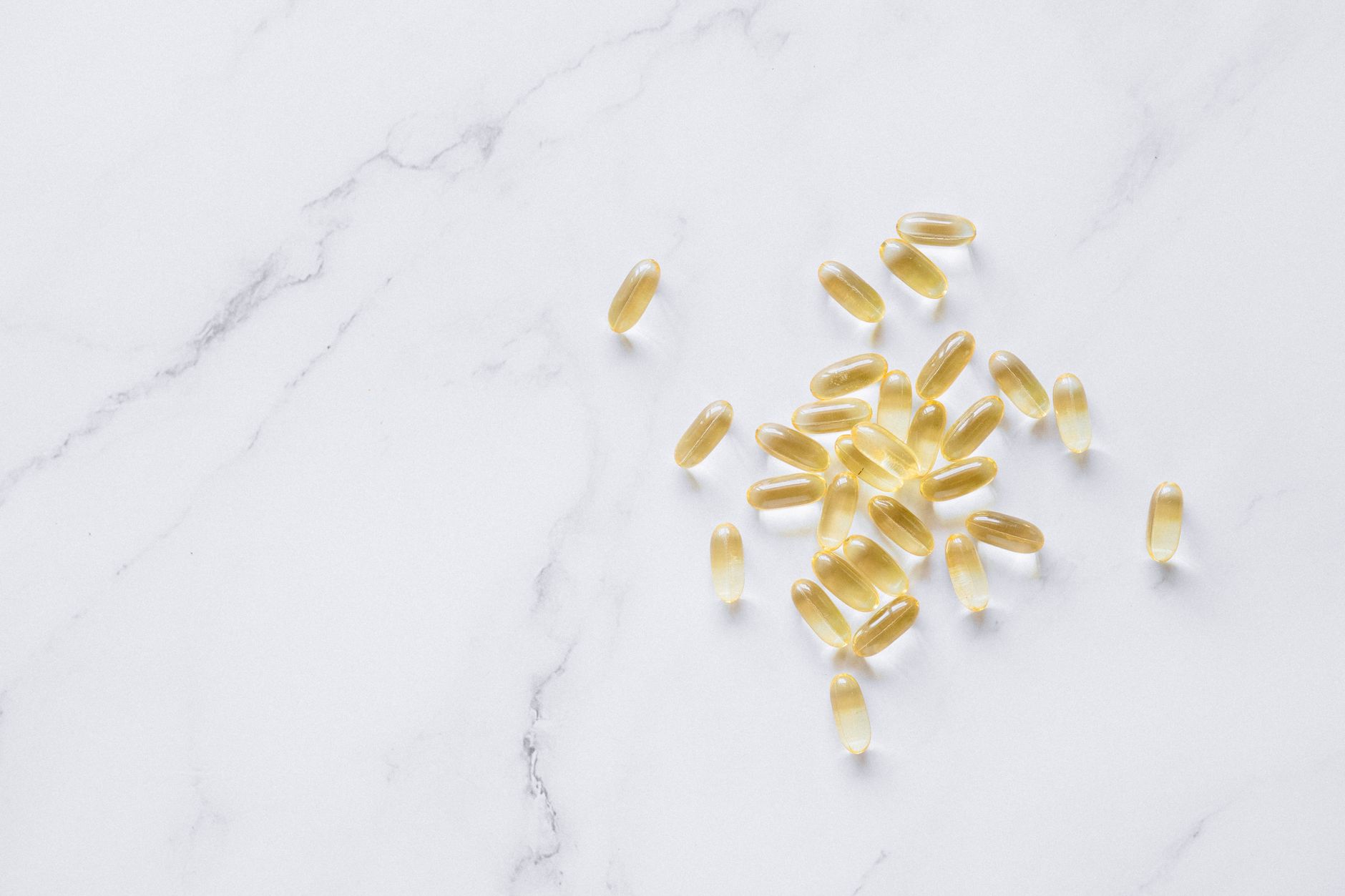 Golden fish oil softgel capsules scattered on a bright white marble surface