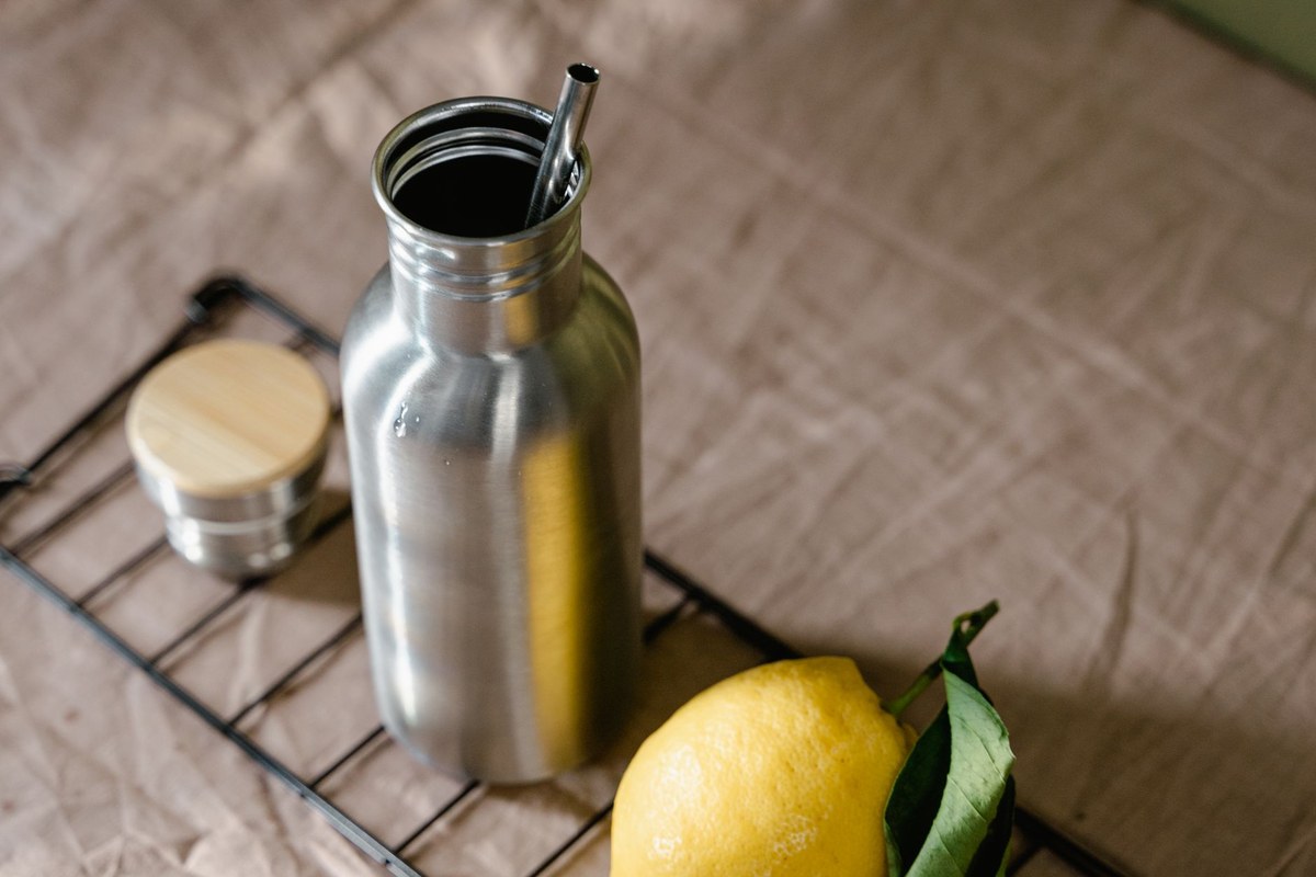 A stainless-steel reusable water bottle with a metal straw and a fresh lemon on a bright table, evoking everyday hydration habits