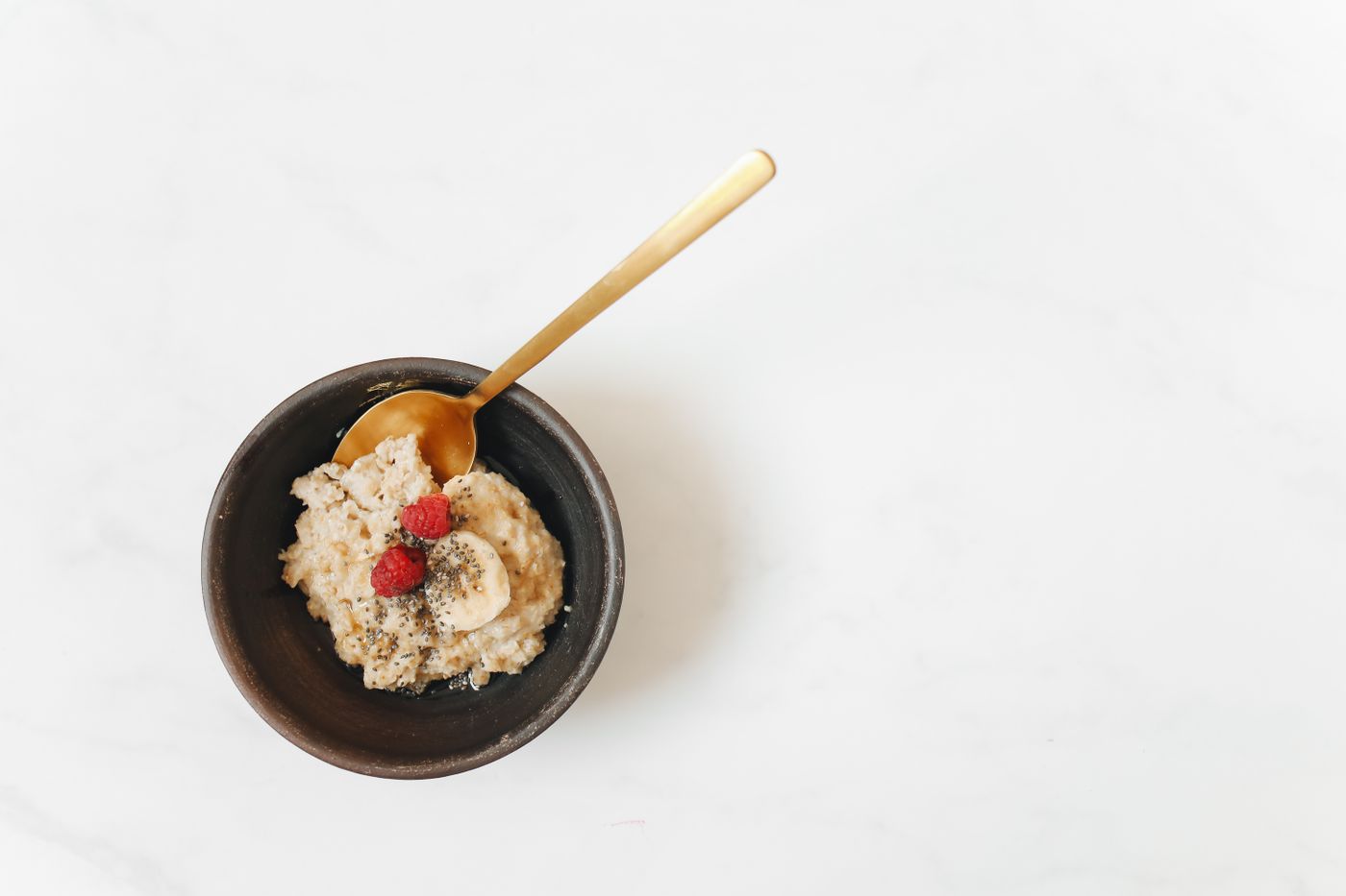 Overhead shot of a reflux-friendly bowl of oatmeal topped with sliced banana and berries on a bright, clean table