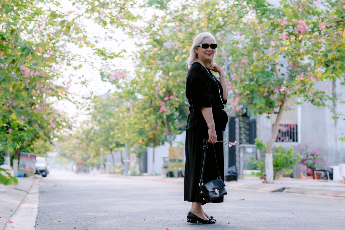 A silver-haired senior woman walking outdoors along a sunny, tree-lined street on a bright morning