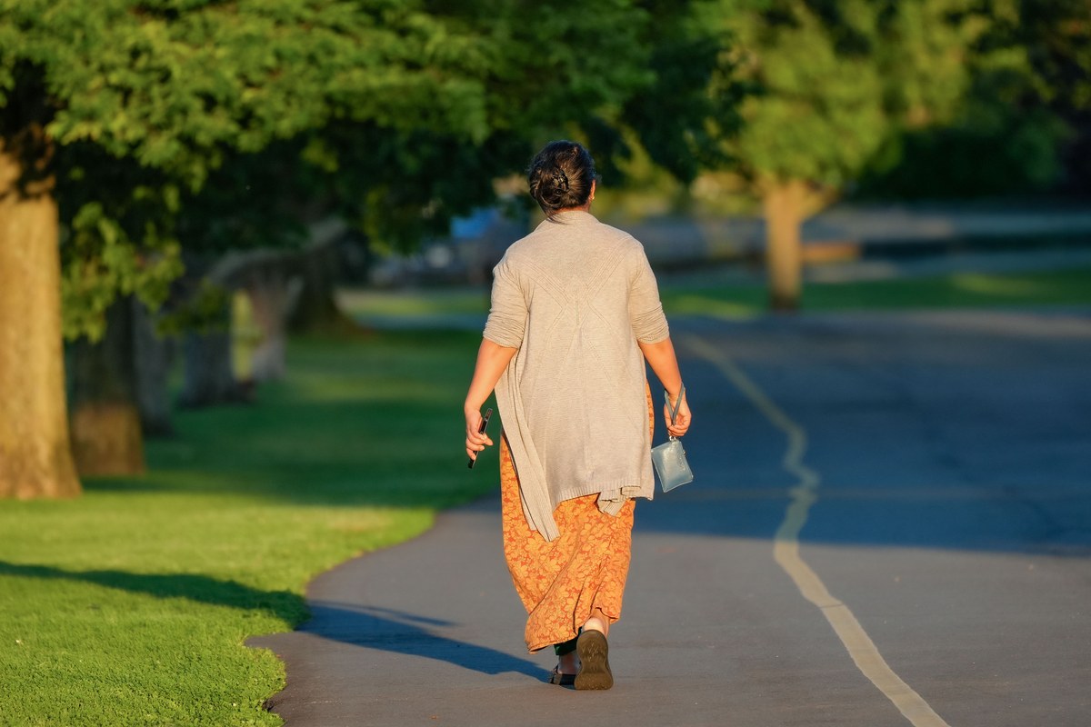 A woman walking outdoors on a tree-lined path in the bright morning light, active and at ease