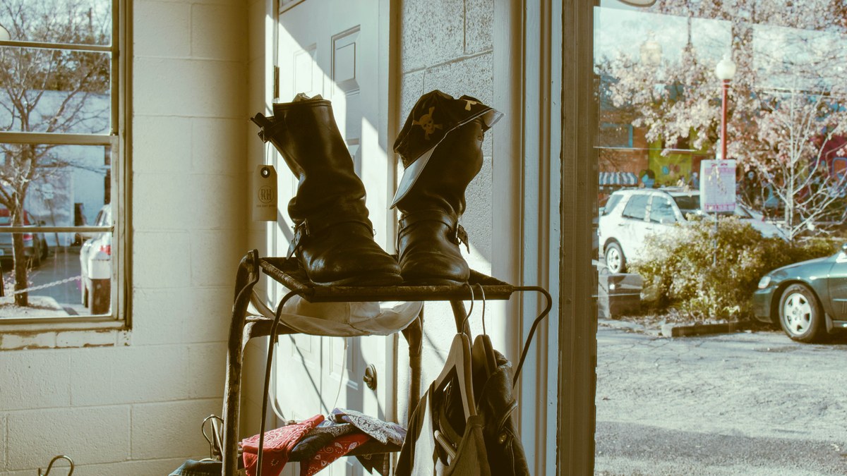 A pair of worn leather boots on a shoe rack beside an open front door, morning light coming in