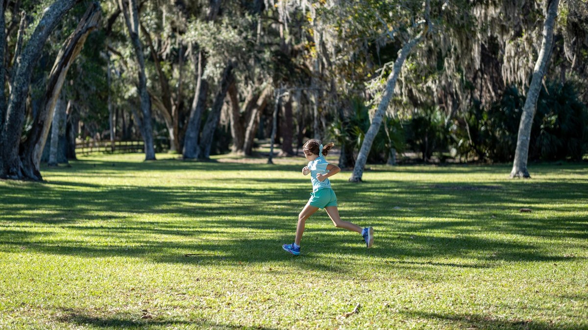 A child running across a sunlit park lawn, the kind of play that brings on coughing or wheezing in a child with asthma