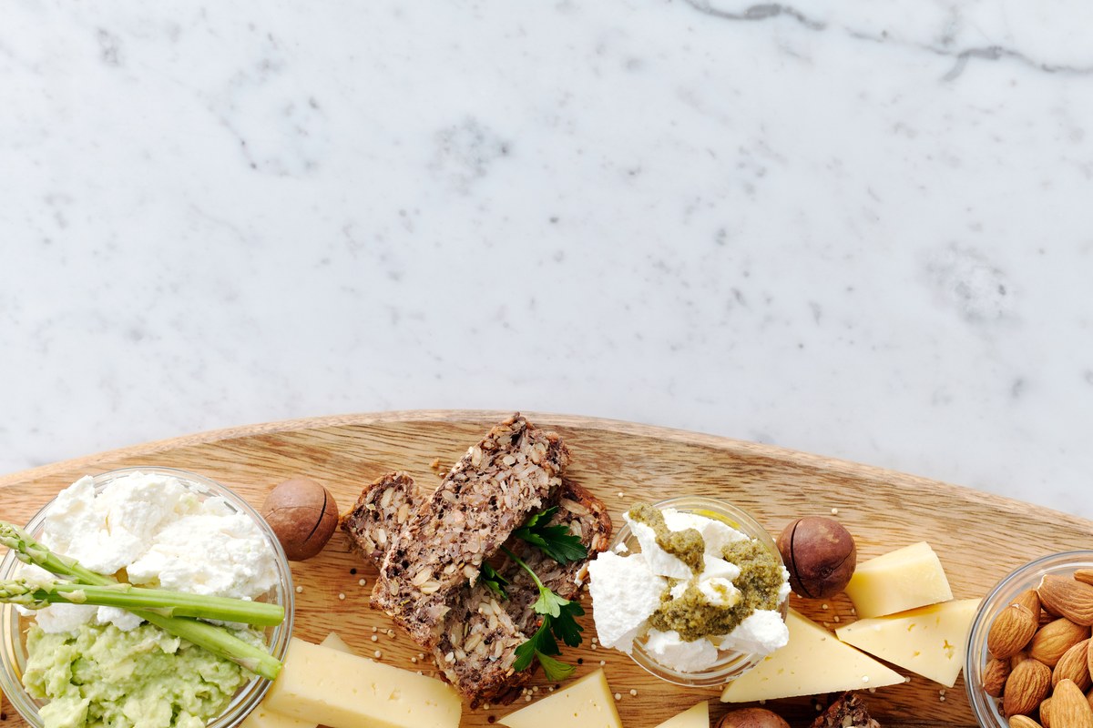 A wooden board of cheese, seeded bread, nuts and olives on a bright marble counter, roughly the size of the snack a few hundred calories buys