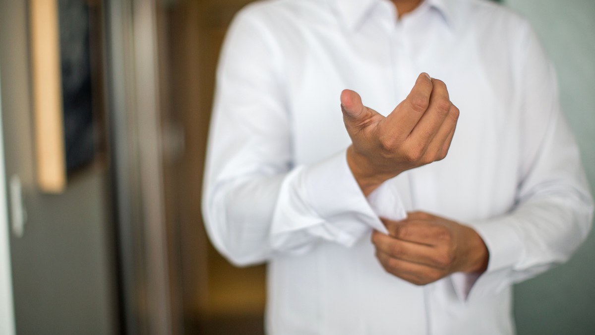 Close-up of a man's hands fastening the cuff button of a white shirt