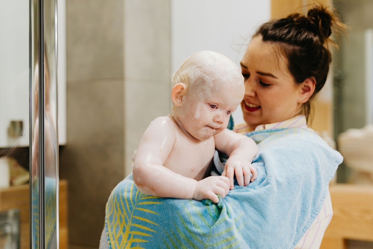 A parent lifting a soapy, damp baby out of the bath wrapped in a soft blue towel