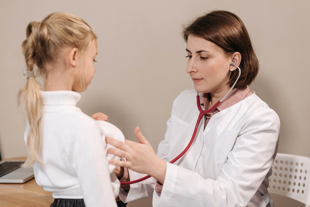 A pediatrician listening to a young girl's chest with a stethoscope during a clinic check-up