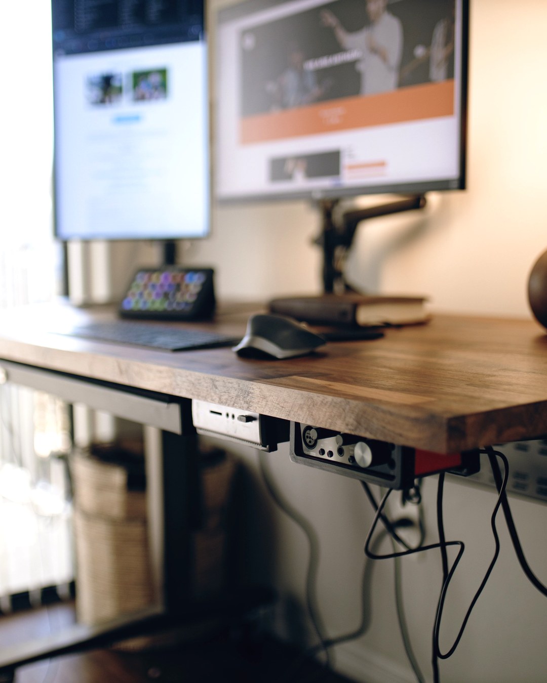 A height-adjustable standing desk with monitors and a keyboard beside a window, no people