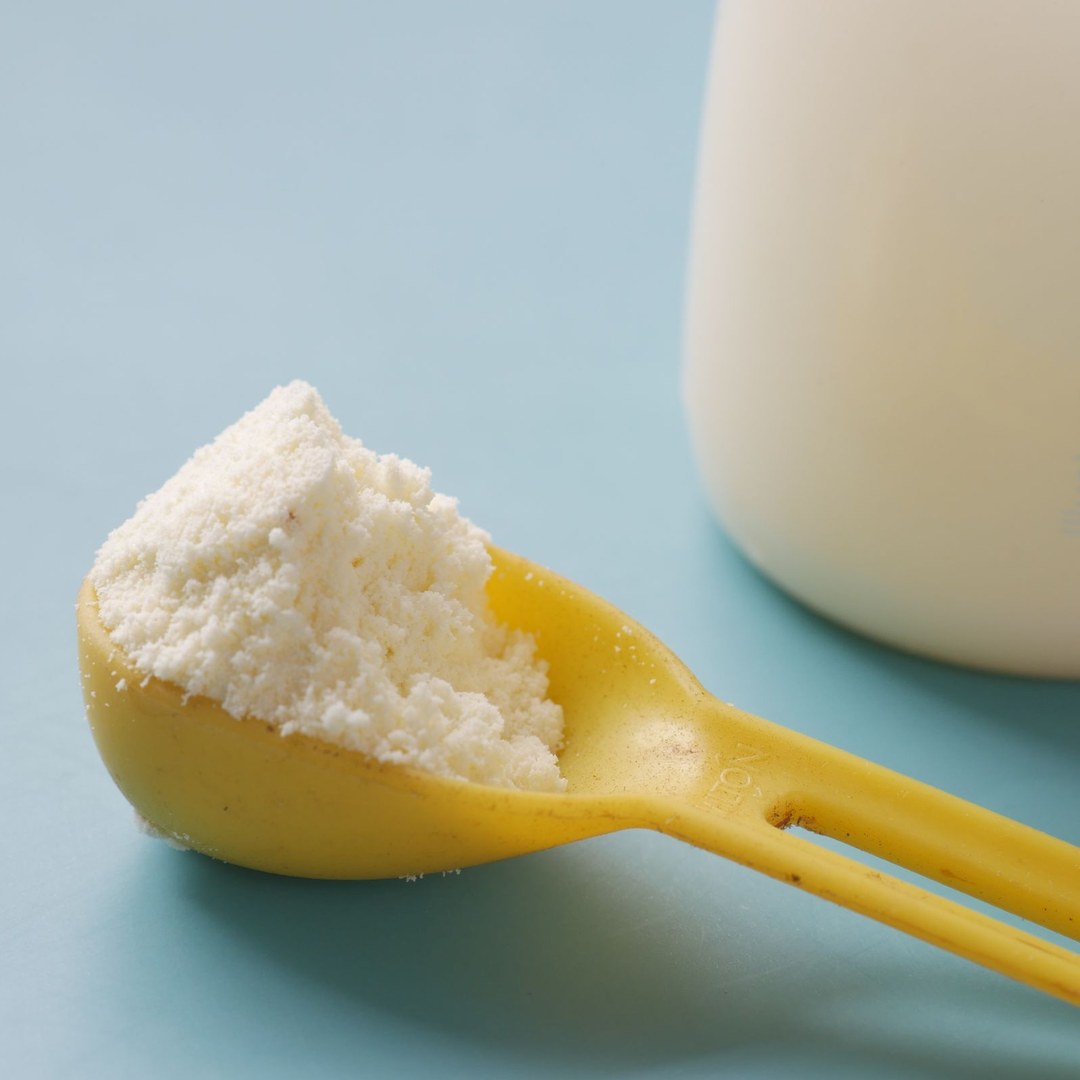 A yellow formula scoop heaped with powder next to a marked measuring bottle, the mix-to-label-directions standard