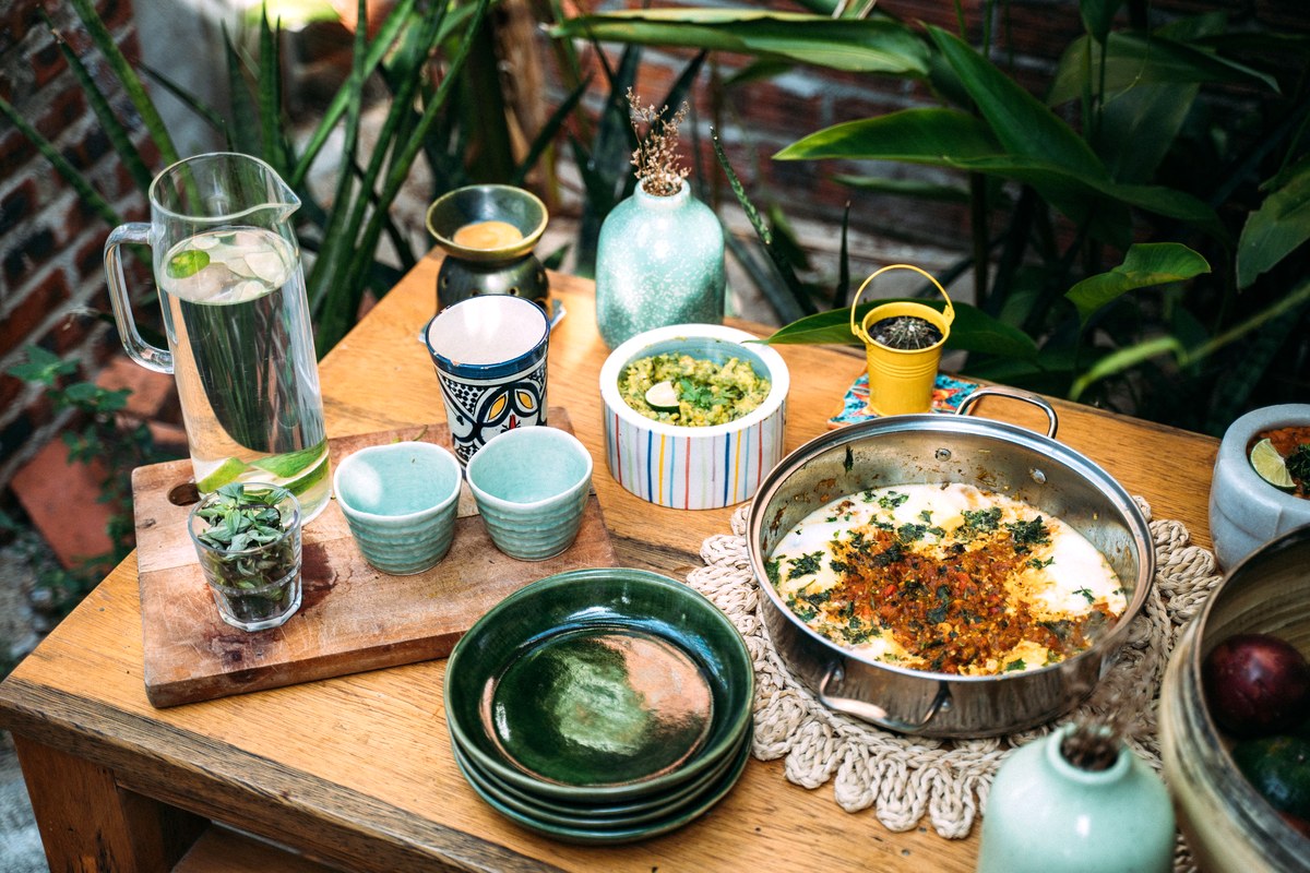 An everyday table set with a pitcher of water, cups and a shared dish of food in bright daylight