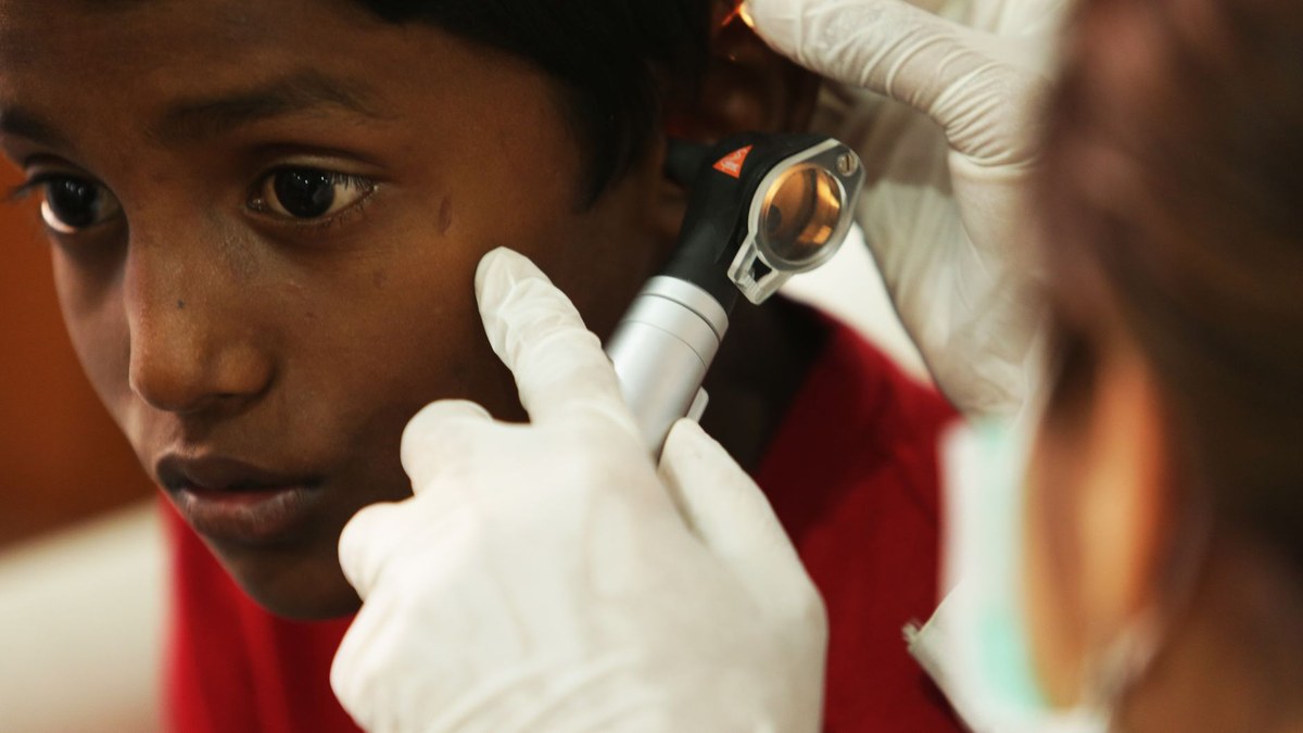 A clinician examines a young child's ear with an otoscope during a checkup