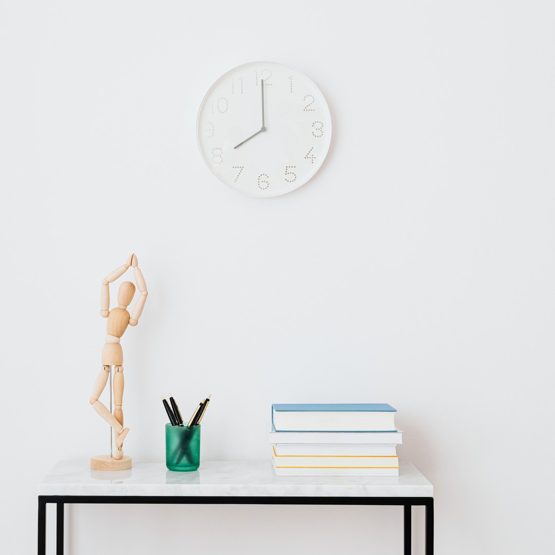 A plain white wall clock above a marble console table with books and pens in a bright, minimal room