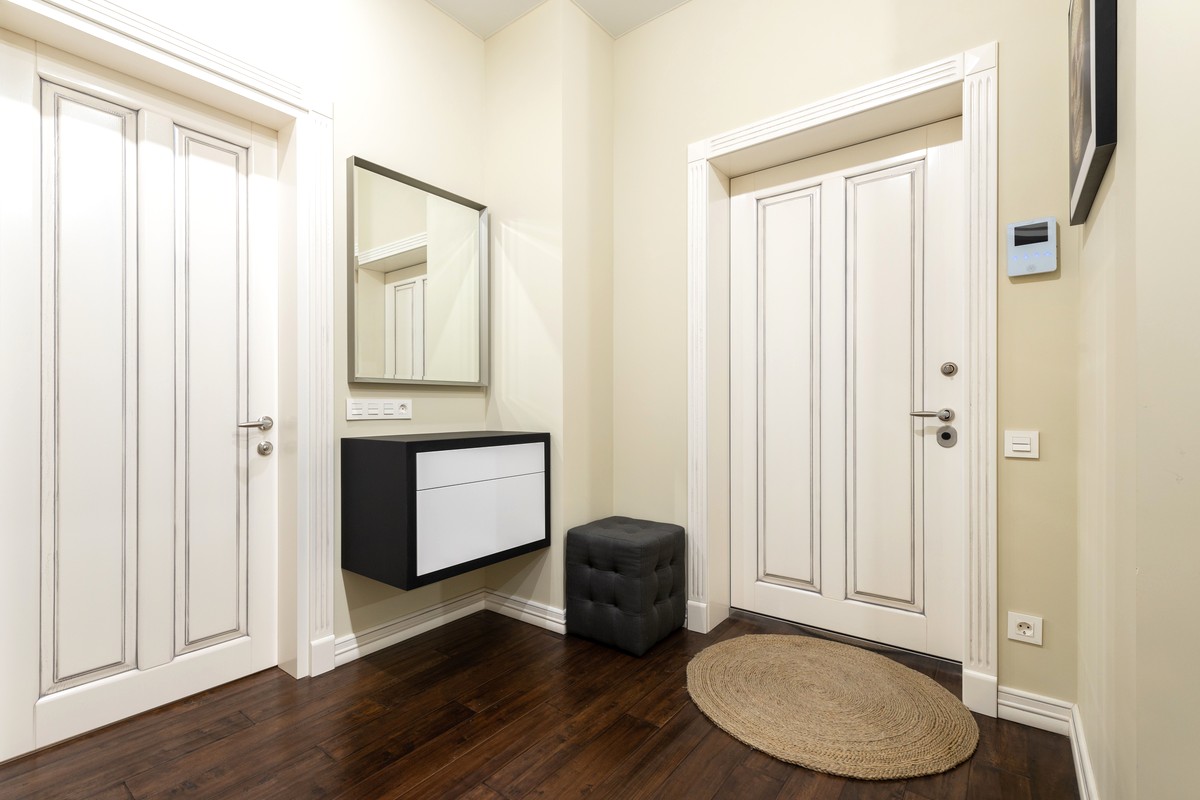 A bright, uncluttered home hallway with pale doors and a round woven rug on the floor