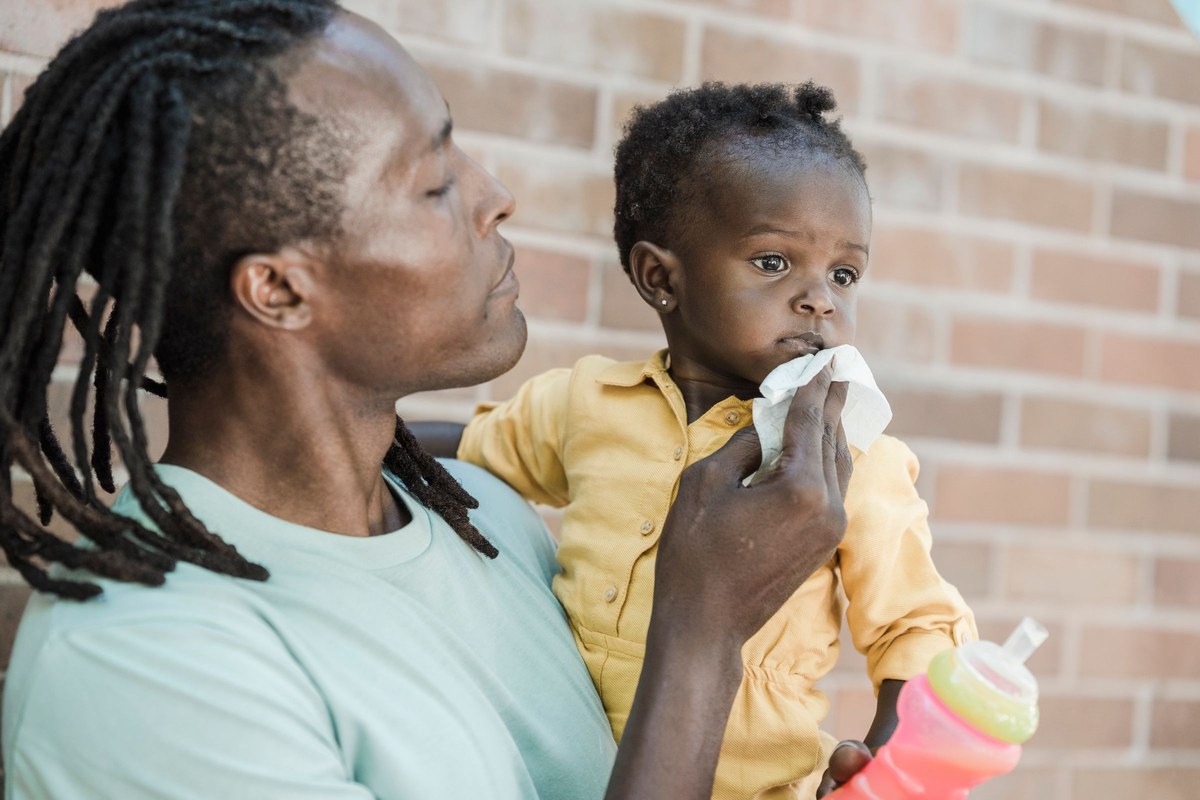 A father holding his toddler on his arm and gently blotting her mouth with a soft tissue, no rubbing