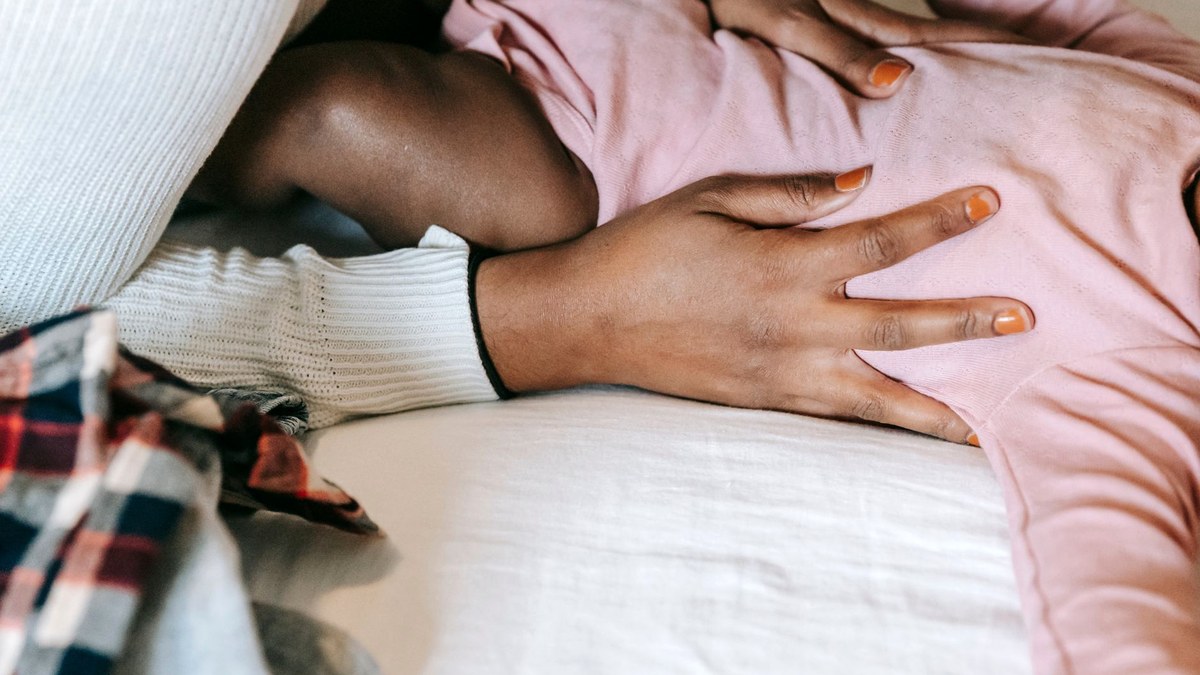 A parent's hands resting gently on an infant lying on a white bed, seen from above, no faces in frame