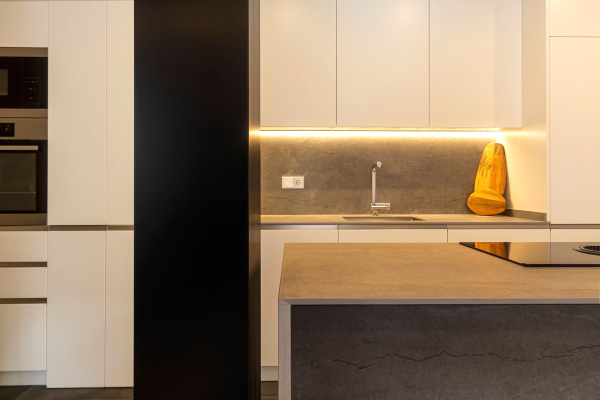 A tidy kitchen at night with the overhead light off, an empty counter lit only by a strip light under the cabinets