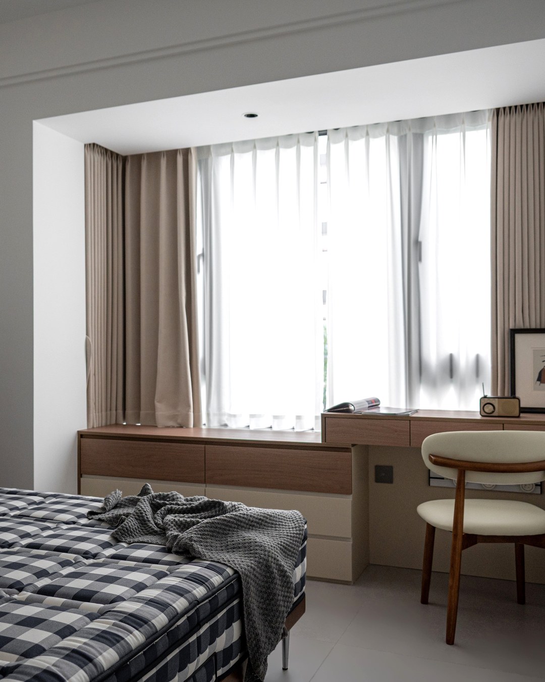 A neatly made bed in a quiet bedroom with daylight coming through sheer curtains, no people