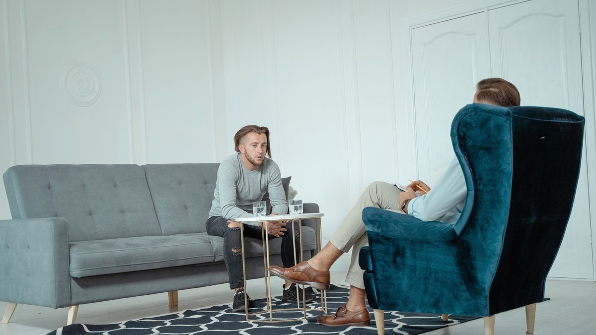 Two men sitting and talking in a calm, uncluttered consultation room with no medical equipment in view
