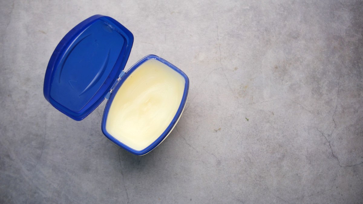 An open tub of plain white petroleum jelly with the lid folded back, seen from above