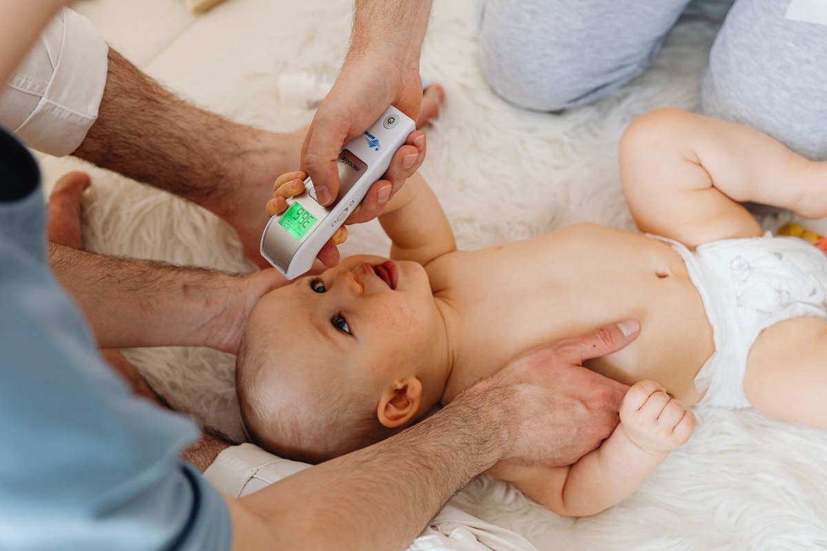 A parent taking a baby's temperature with a digital forehead thermometer on a soft white blanket