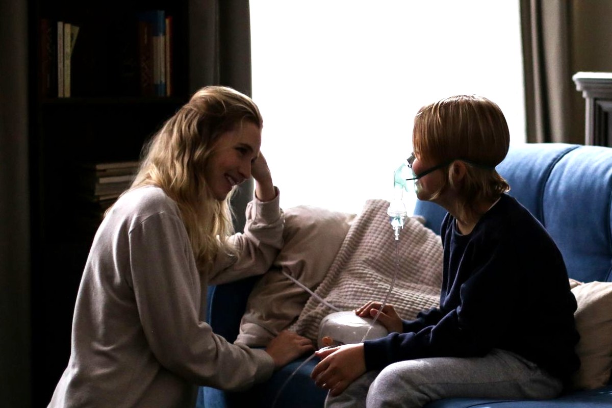A parent kneeling beside a child on the sofa who is breathing through a home nebulizer mask