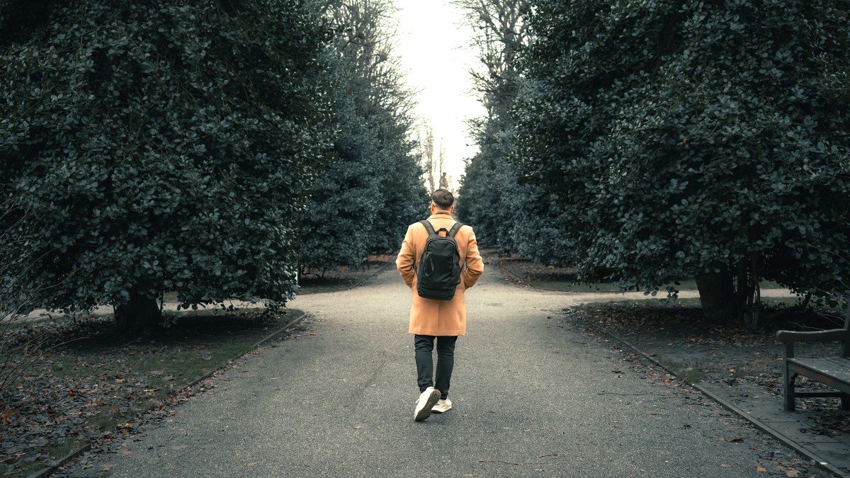 A man in a yellow coat walking away along a tree-lined park path in the morning