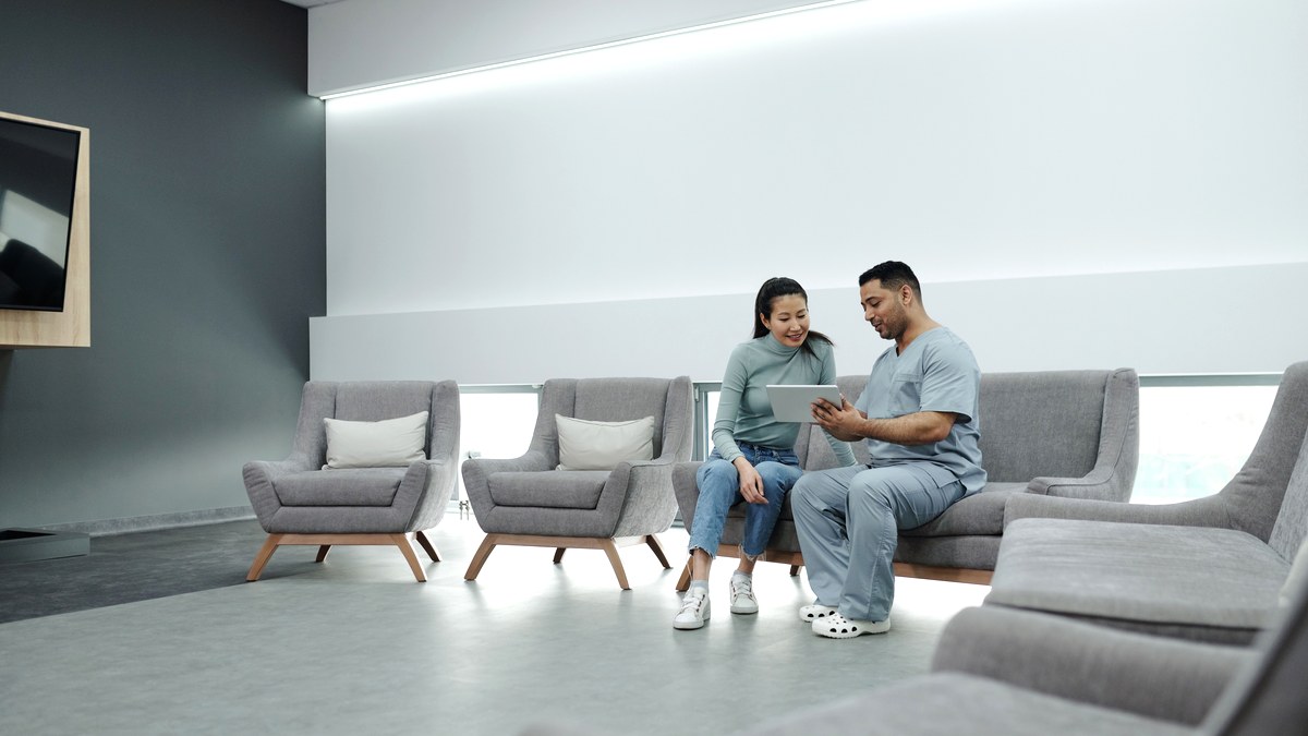 A clinician and a patient sitting together in a bright, uncluttered clinic room, talking through results on a tablet