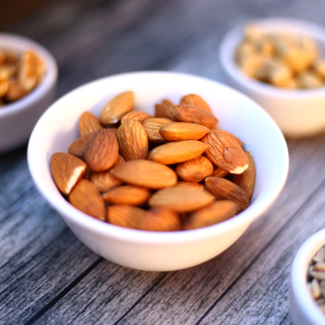 A white ceramic bowl of whole almonds on a wooden table