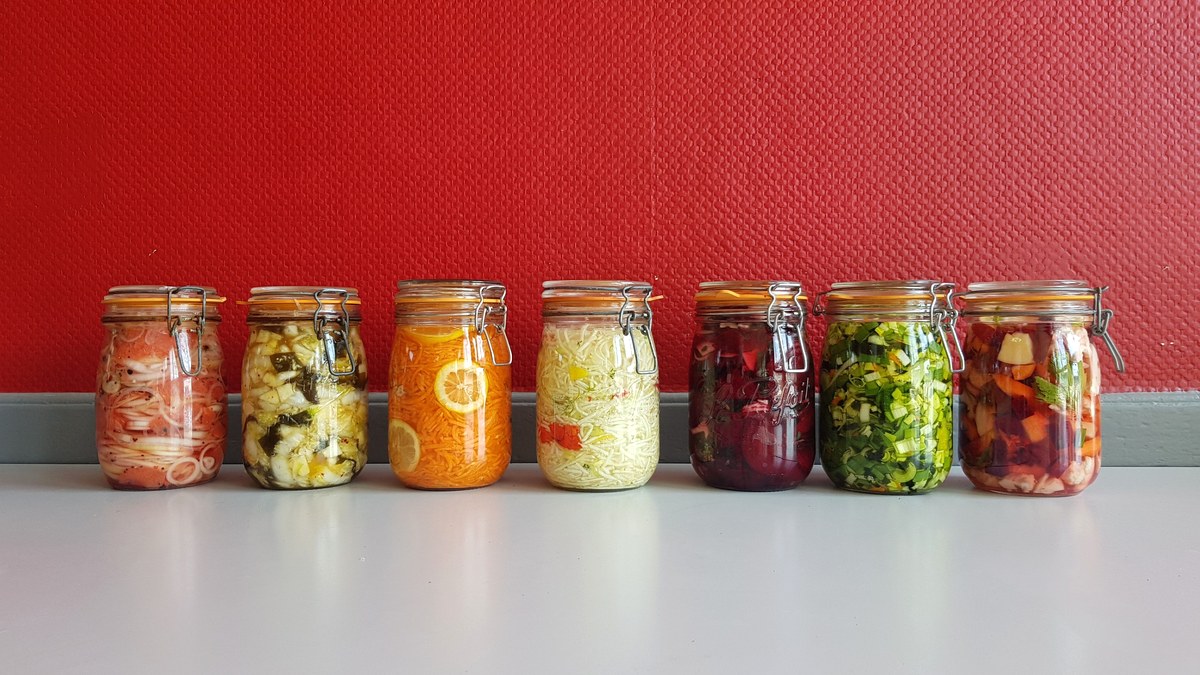 A row of glass mason jars of colourful fermented vegetables lined up on a shelf
