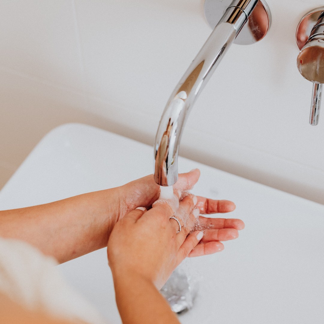 Close-up of soapy hands being rinsed under a running tap at a white bathroom sink