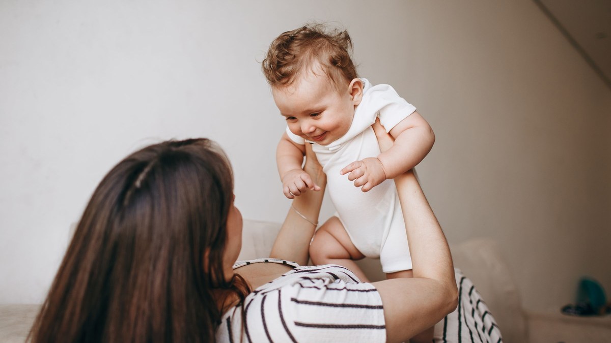 A parent lifting a smiling baby up in a bright, plain room