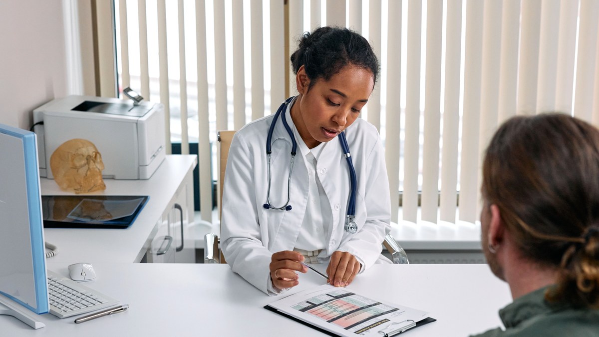 A clinician sitting across a desk from a patient in a bright office, going through a printed chart together