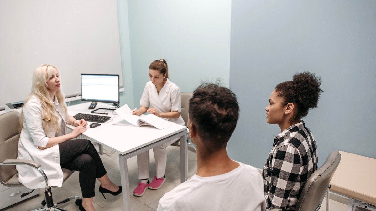 Two people sitting across a desk from a clinician in a bright consultation room, talking through results